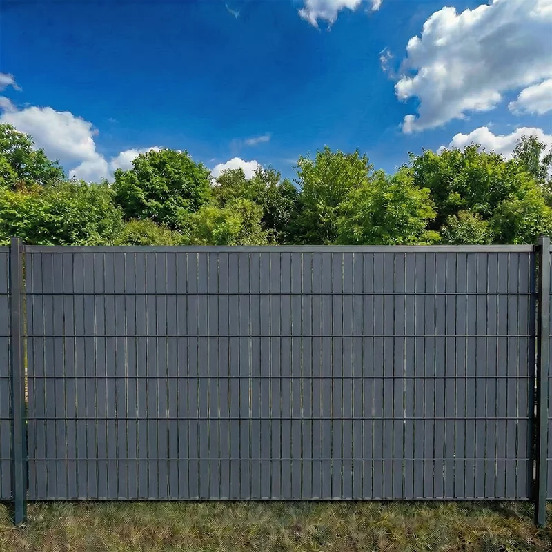 Flexio Schieferfarbener Sichtschutzstreifen im Doppelstabmattenzaun als Sichtschutz im Garten bei blauem Himmel und Bäumen.