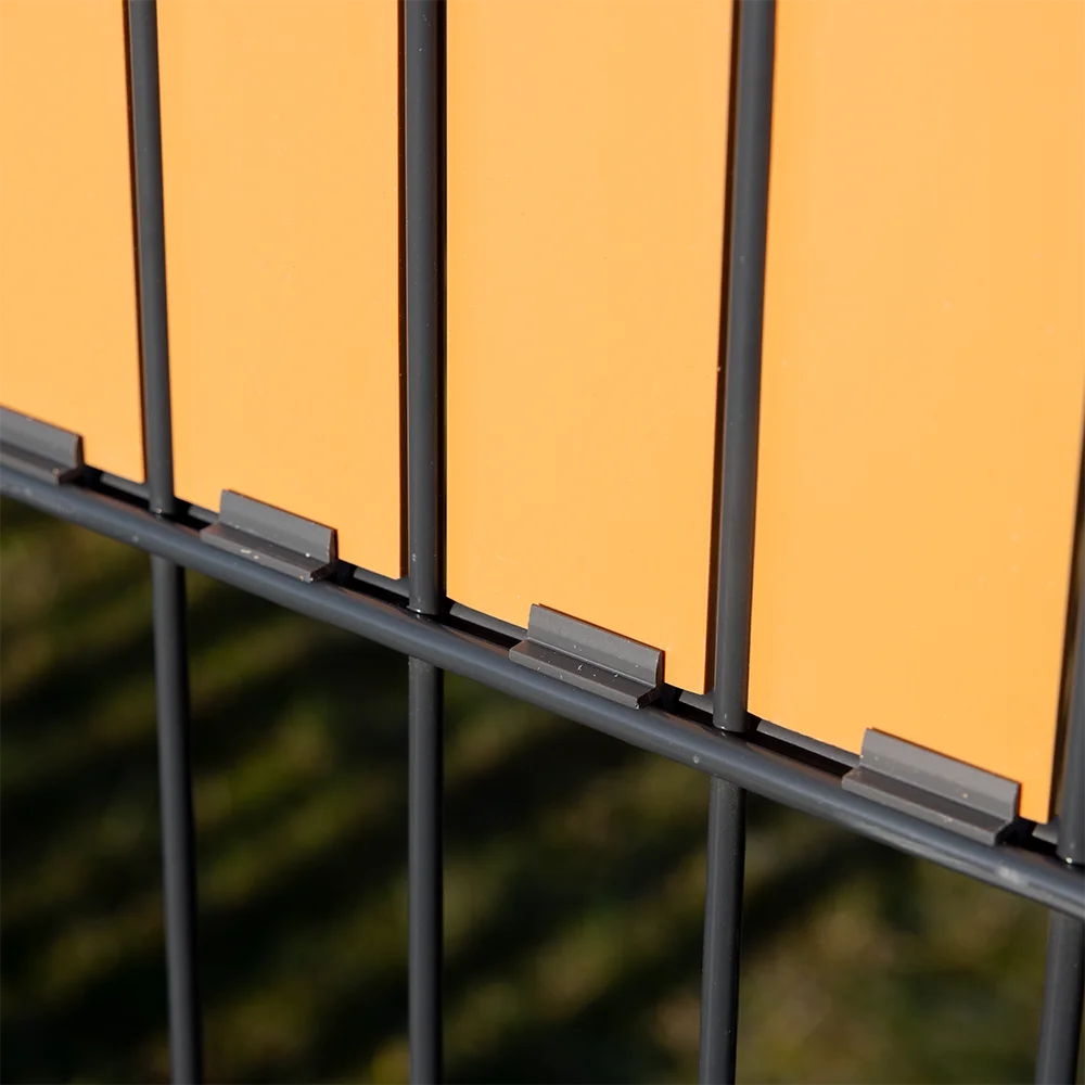 Detailansicht eines modernen Doppelstabmattenzauns mit bernsteinfarbenen Sichtschutzpaneelen und Befestigungsclips von Wodewa